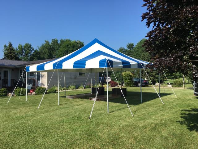 20x20 Blue and White pole tent setup on grass with tables and chairs placed under tent with house and trees in background.